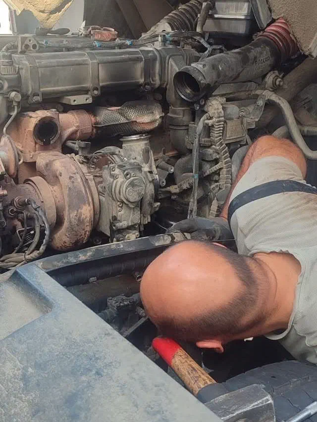 Mechanic working on a truck engine from behind the cab